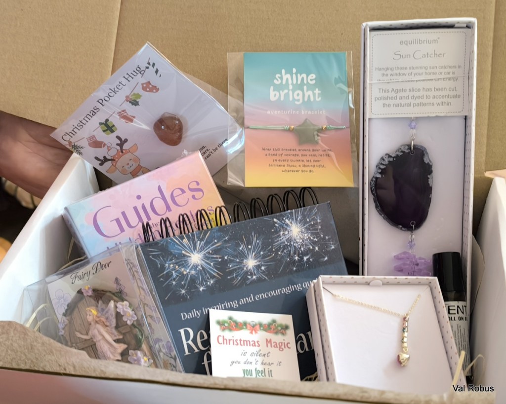 A gift box filled with various items including a Christmas Pocket Hug, an aventurine bracelet, a sun catcher, and a fairy-themed decorative piece, all arranged thoughtfully.
