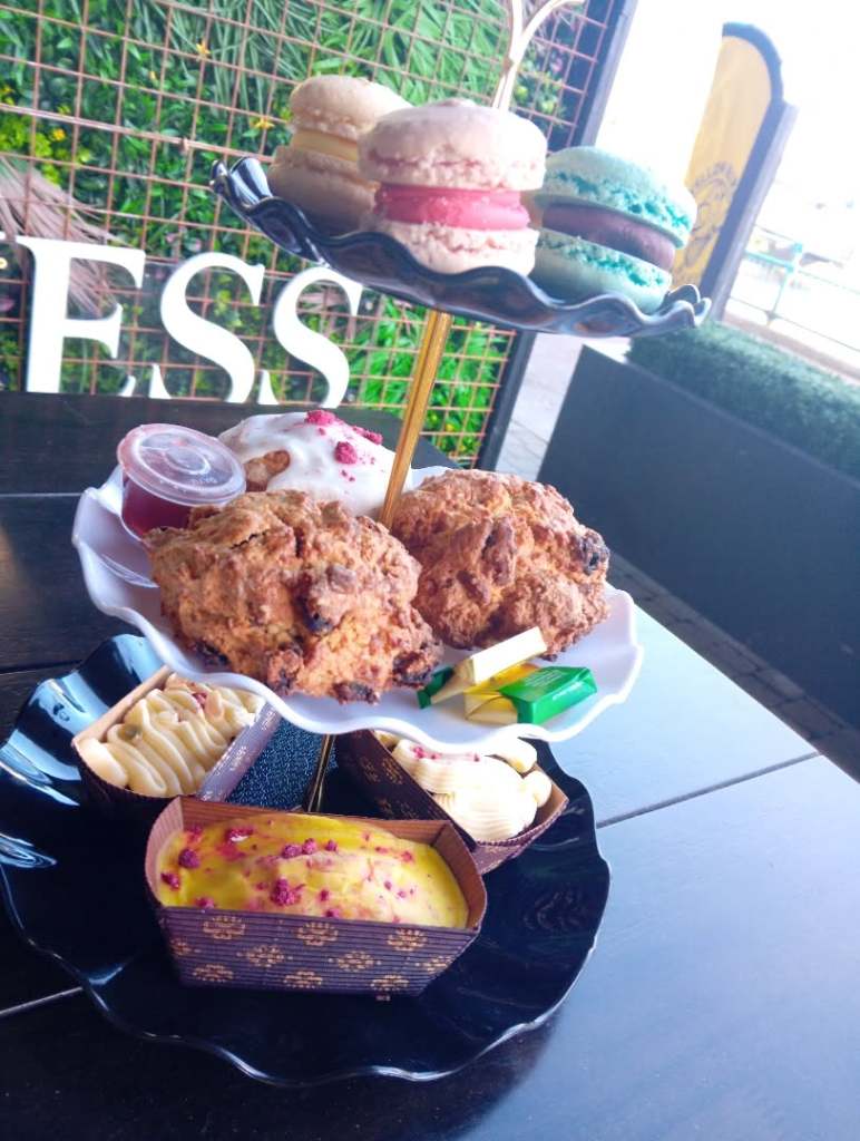 A tiered dessert display featuring colorful macarons, cookies, and assorted cakes, served on a black plate.