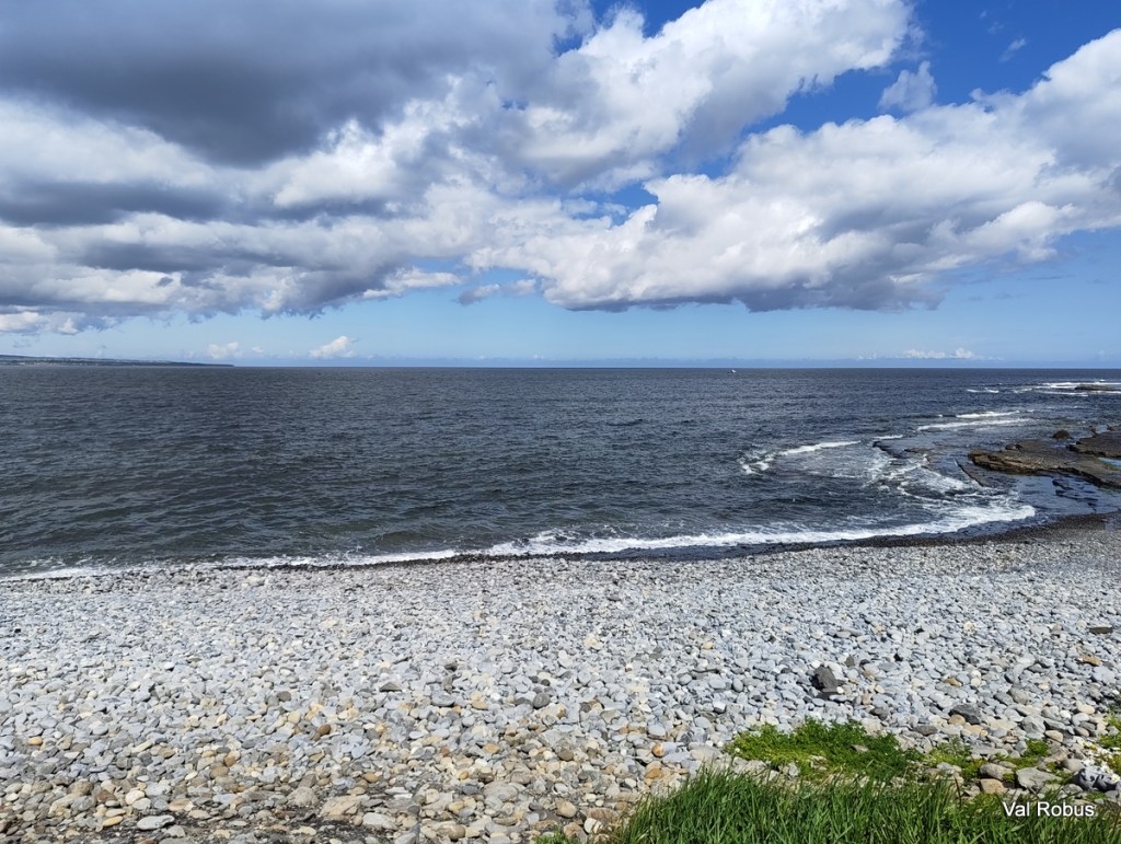 A scenic view of a rocky beach with waves lapping at the shore under a partly cloudy sky.