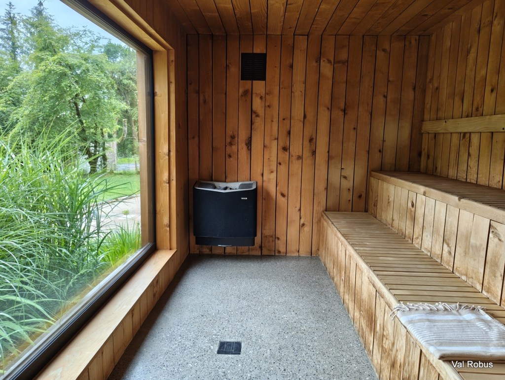 Interior of a sauna with wooden walls and benches, featuring a large window that overlooks greenery outside.