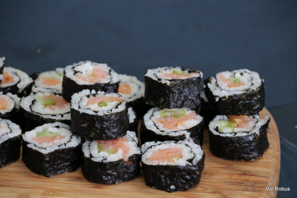 A close-up view of sliced sushi rolls arranged on a wooden board, featuring rice, salmon, and green vegetables wrapped in nori.