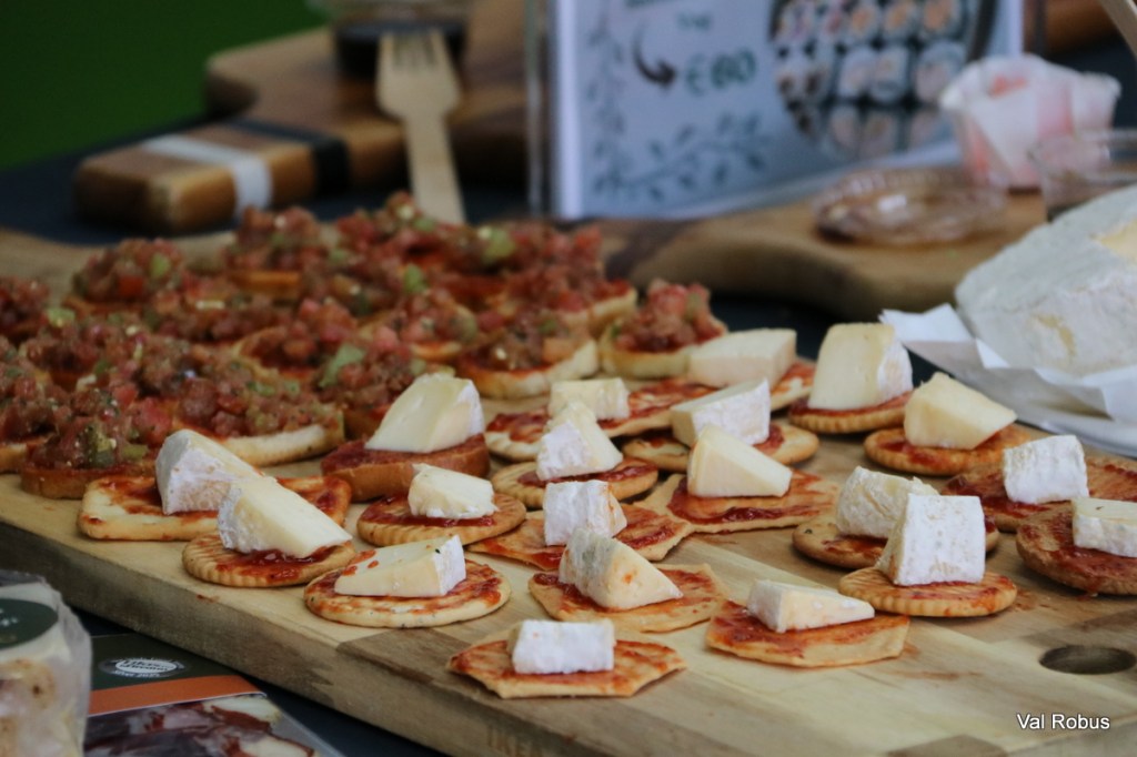 A wooden platter displaying various appetizers, including crackers topped with cheese and spreads, and small portions of chopped meat and vegetables.