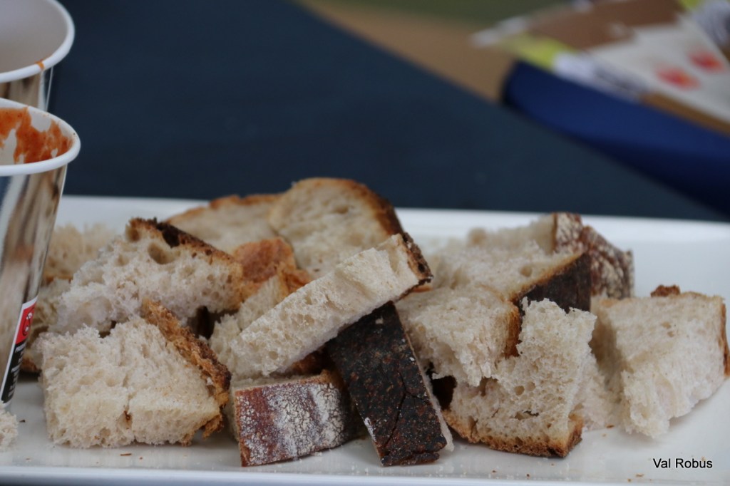 A plate of cut bread pieces, showcasing a mix of light and dark crusts, with a cup of red sauce in the background.