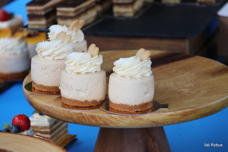 Mini cheesecakes topped with whipped cream and almond slivers, displayed on a wooden cake stand.
