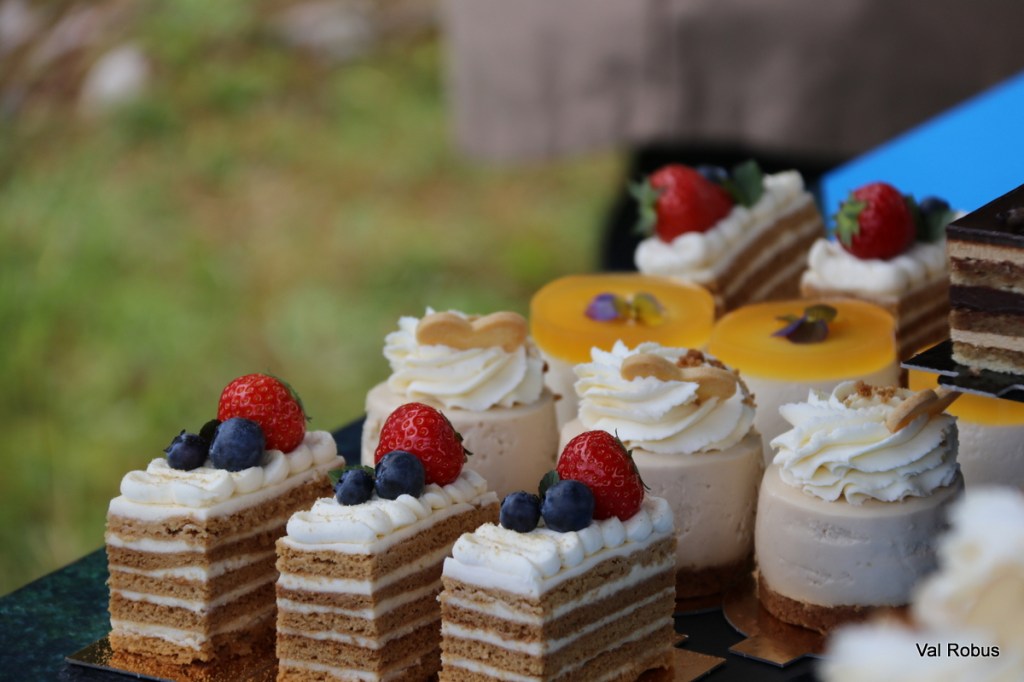An array of beautifully decorated miniature cakes featuring layers of cream, topped with fresh berries and edible flowers.