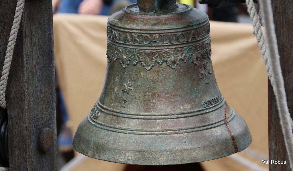 Close-up of an antique bell engraved with 'Andalucia' and decorative elements, hung on a wooden support.