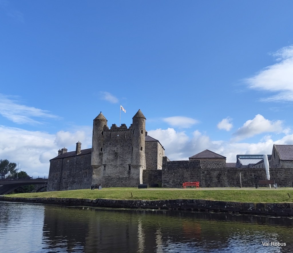 Historic stone castle with turrets beside a river under a blue sky.
