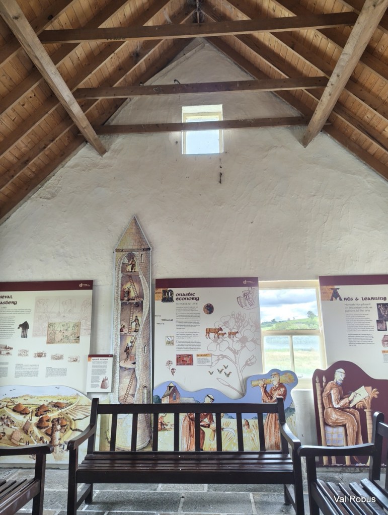 Interior view of a historical exhibit space showcasing educational panels on medieval monastic life, with wooden beams and benches.