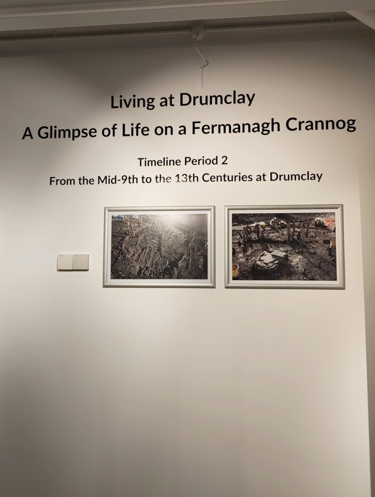 Exhibition title 'Living at Drumclay: A Glimpse of Life on a Fermanagh Crannog' with timeline details and two framed photographs.