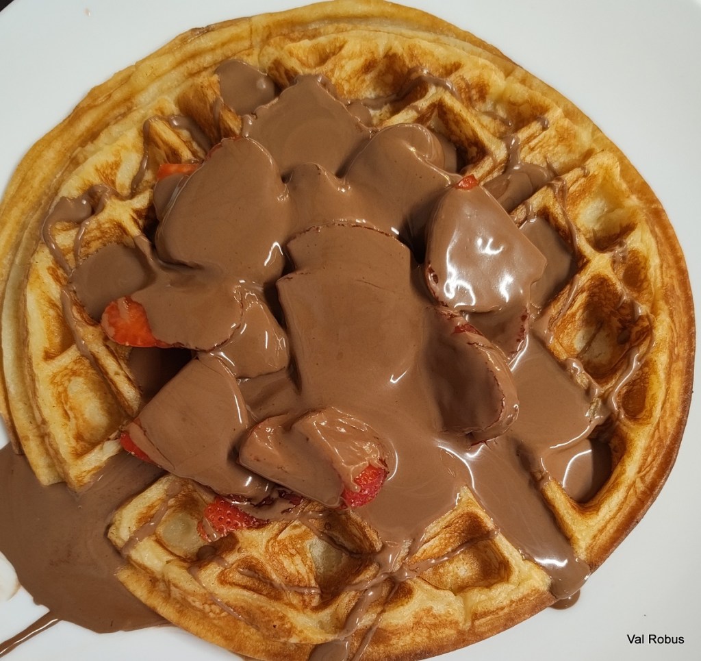 Close-up of a waffle topped with melted chocolate and sliced strawberries.